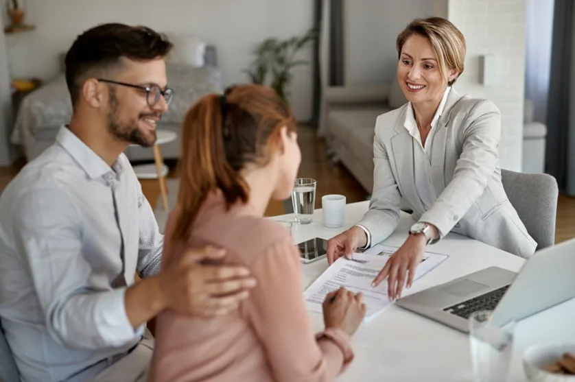 An agent meeting with a young couple and pointing to a place to sign on a contract.
